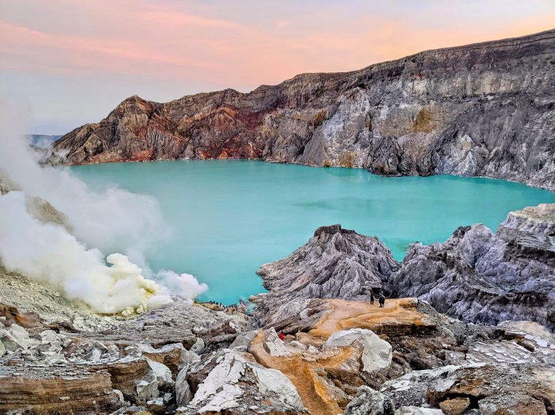 The sunrise at Ijen Crater has purple and orange skies with the turquoise lake and sulfur smoke