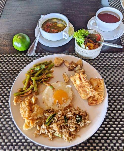 A plate of fried rice, fried tempeh and fish, egg, and green beans with a side of soup and tea for breakfast at Ketapang Indah Hotel