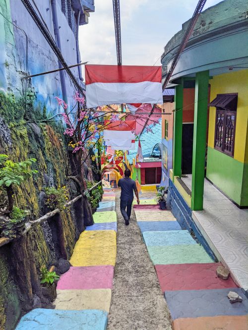 A man walks down a road with colorful stairs and a red and white Indonesian flag at Malang Colorful Houses