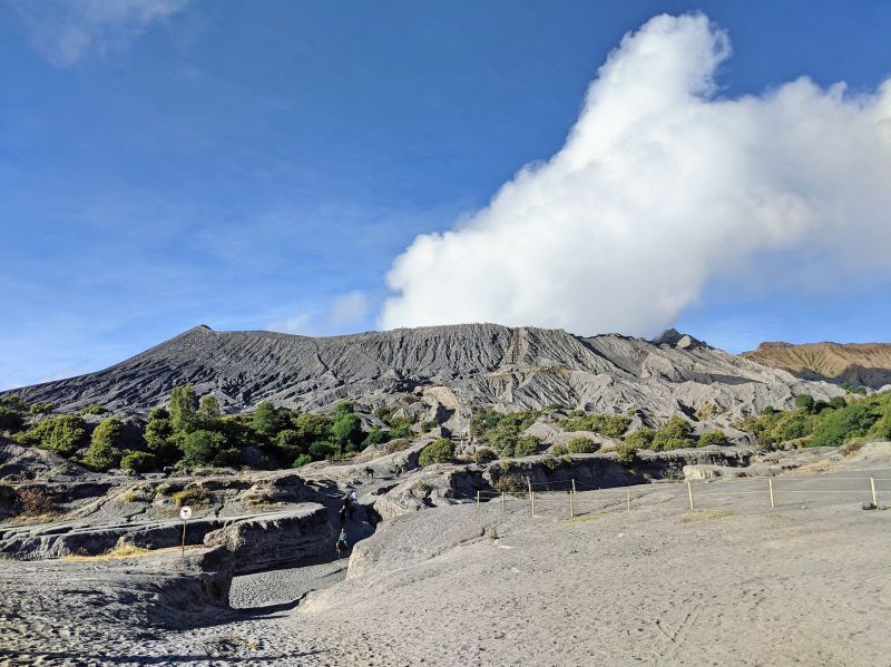 A landscape view of Mount Bromo volcano with the grey sand and the crater expelling smoke