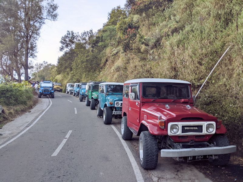 8 colorful Jeeps from red, blues, and greens park along the road while waiting for visitors at Bromo sunrise