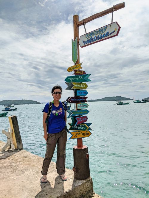 Jackie Szeto, Life Of Doing, stands next to a sign with directions to landmarks at Huy Hoang Hotel