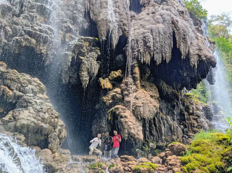 Justin Huynh, Jackie Szeto, and Arief, tour guide, stand in a cave next to Goa Tetes Waterfall