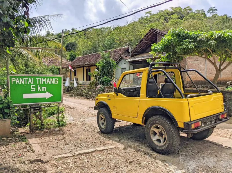 A yellow Jeep parks next to the Pantai Timang 5km sign