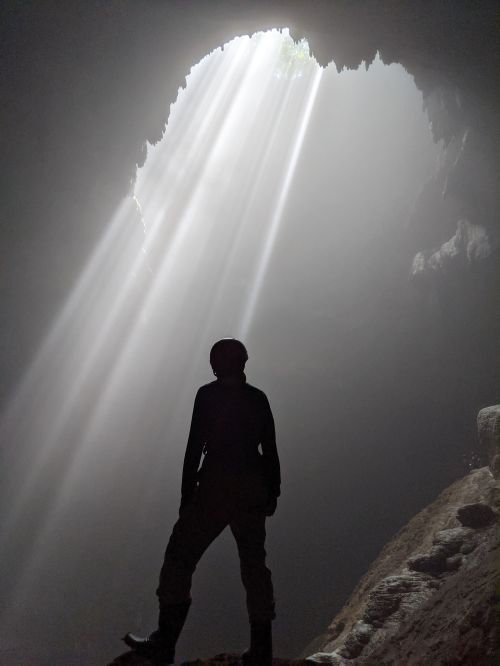 Justin Huynh, Life Of Doing, stands on a rock with the morning rays shining into the Jomblang Cave