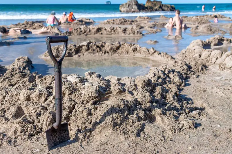 A shovel standing up in the Hot Water Beach and shallow pools of hot water at Coromandel Peninsula, North Island New Zealand
