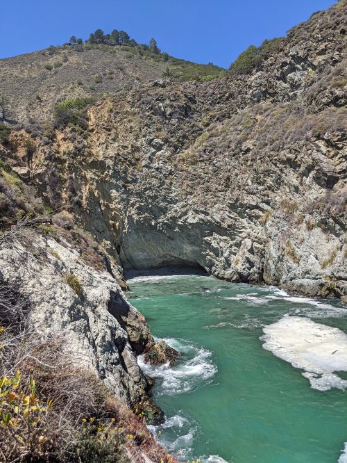 Teal colored ocean water flowing into a rocky cove area of Partington Cove, Big Sur, California