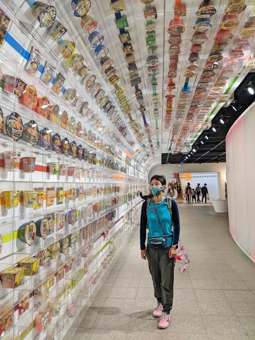 Jackie Szeto, Life Of Doing, walks along the ramen tunnel with a wall of Nissin products and instant noodles