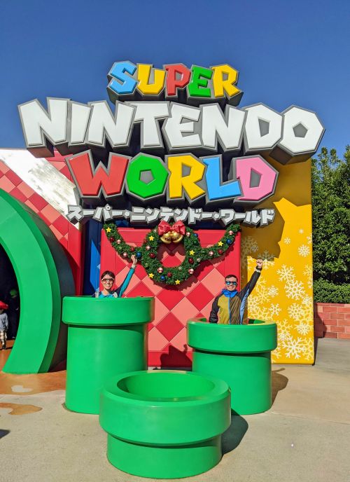 Jackie Szeto and Justin Huynh, Life Of Doing, hold their hands in the air while posing with the Super Nintendo World sign at Universal Studios Japan