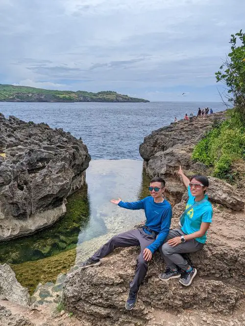 Justin Huynh and Jackie Szeto, Life Of Doing, raise their hands out to the Angel's Billabong pool of water in Nusa Penida, Indonesia