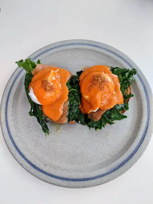 A grey plate with eggs benedict with sourdough toast, wilted kale, smoked salmon and gochujang hollandaise sauce at Baked in Canggu