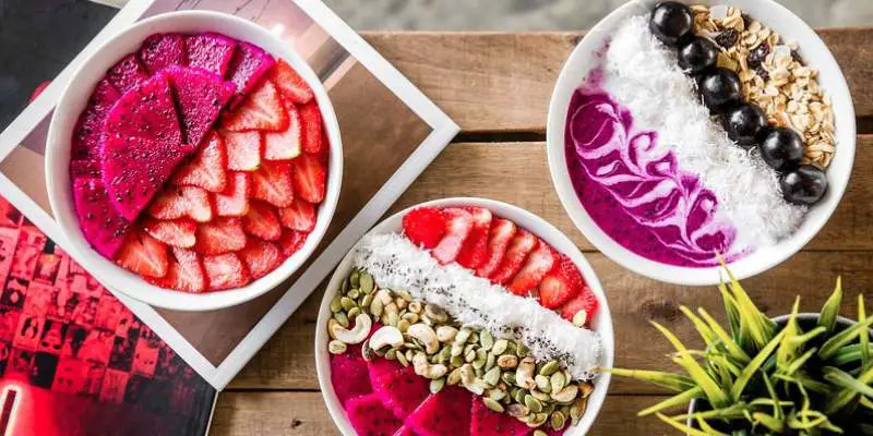 Three smoothie bowls with strawberries, purple dragon fruit, nuts, and other healthy toppings at Crate Cafe, Canggu