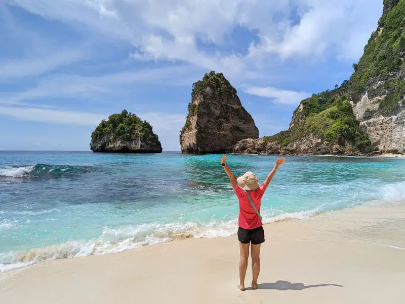 Jackie Szeto, Life Of Doing, holds her hands up in the air on a white sandy beach, Diamond Beach, on Nusa Penida