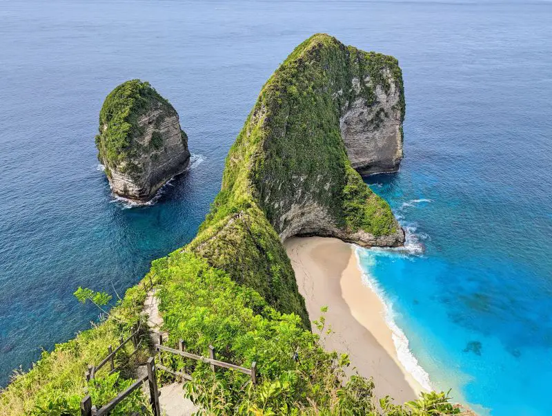 A staircase along the green cliffside with a white sandy beach at Kelingking Beach, Nusa Penida, Indonesia