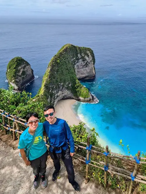 Jackie Szeto and Justin Huynh, Life Of Doing, stand at the best photo spot of Kelingking Beach with the cliffside and beach in the background
