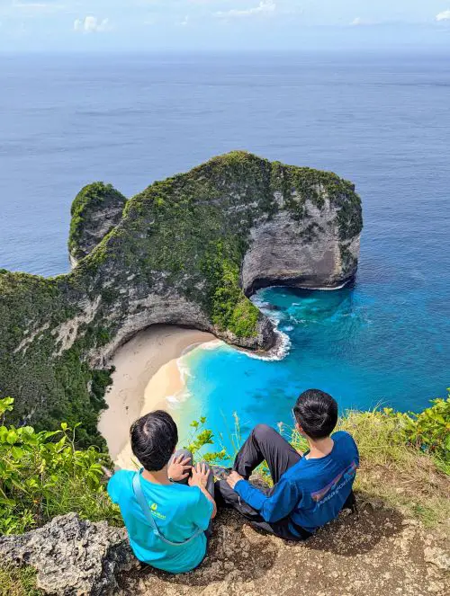 Jackie Szeto and Justin Huynh, Life Of Doing, sit on the edge of the cliff and sees the right side of Kelingking Beach, Nusa Penida
