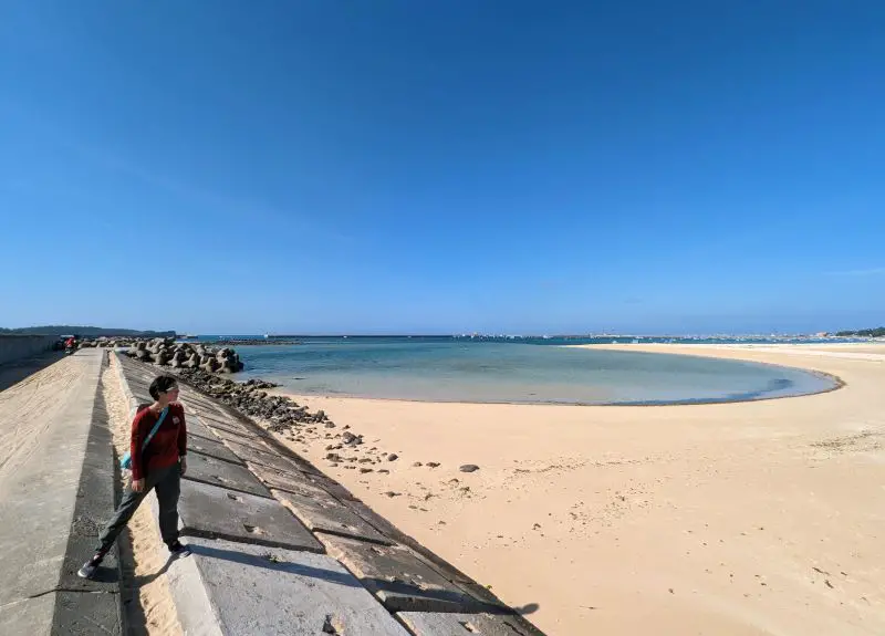 Jackie Szeto, Life Of Doing, stand on a concrete wall next to a clean beach and small ocean at Chaoyang Bay, Phu Quy Island