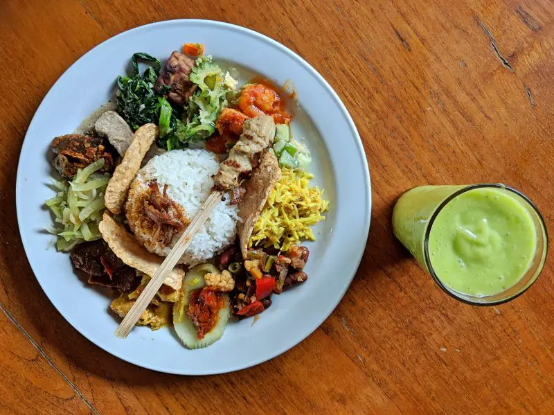 A plate with rice, vegetables, chicken skewer, and an avocado drink at Made's Warung, one of the cheaper restaurants in Seminyak, Bali