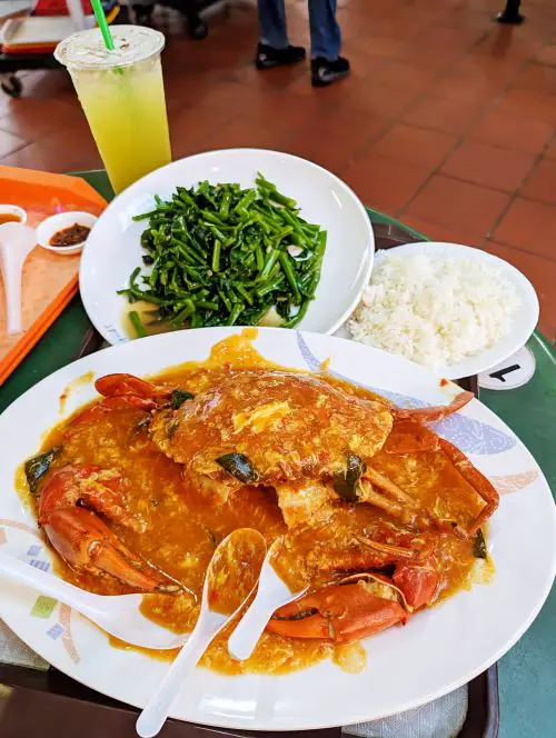 A plate of chili crab with a side of rice and stir fry green vegetables at Maxwell Hawker Centre in Singapore