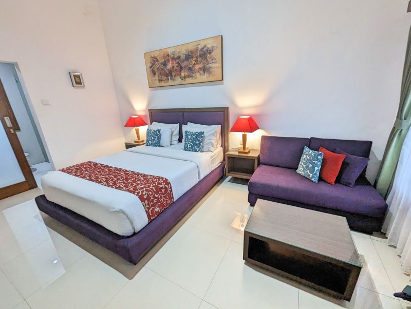 A room at Dikubu Belong Seminyak has a bed with a purple sofa and coffee table
