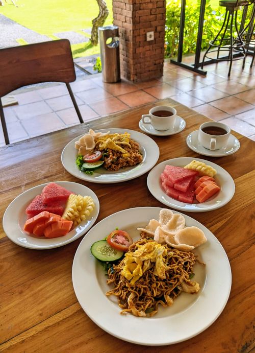 Two plates of tropical fruits, one plate of fried noodles, and one plate of fried rice for breakfast at Kubu Cempaka Seminyak, Bali