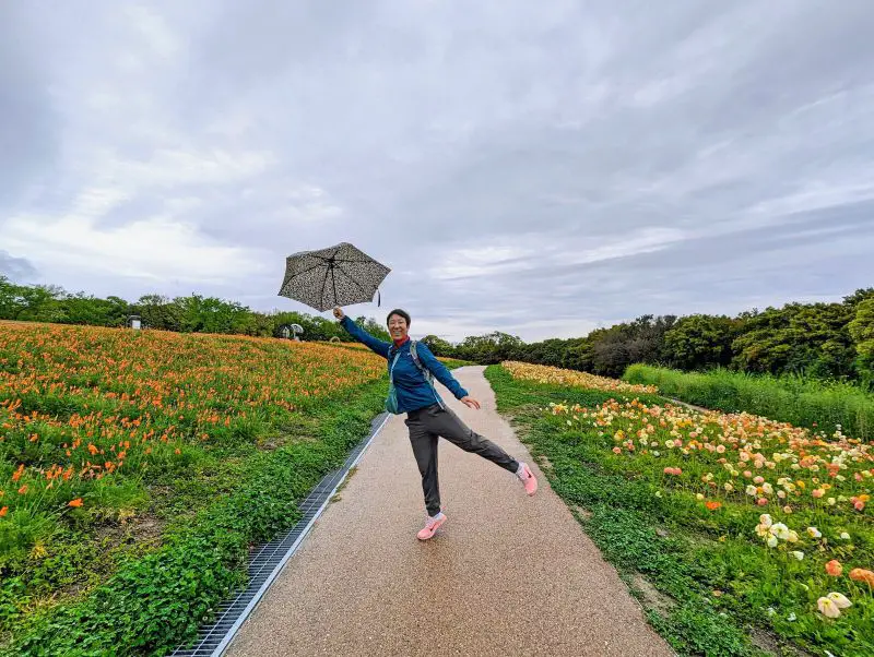 Jackie Szeto, Life Of Doing, holding an umbrella and balancing on one foot along the Flower Hill walking path at Expo 1970 Commemorative Park