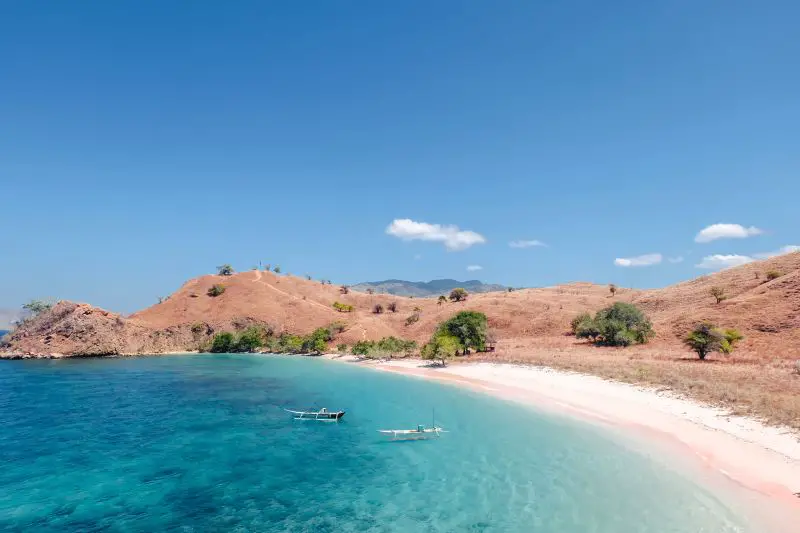 Two boats in the blue waters and next to the pink sandy beach in Komodo National Park, Indonesia