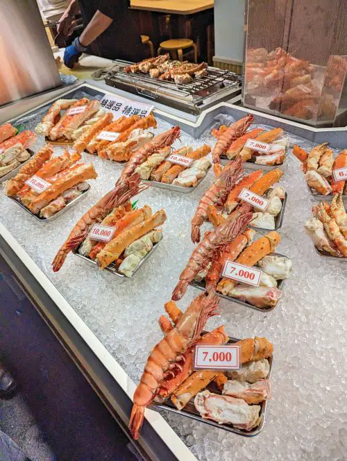 Small trays of fresh lobster, crab, and other seafood for sale at one of the seafood shops in Kuromon Market, Osaka
