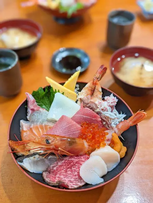 A bowl of freshly sliced sashimi of scallops, sweet shrimp, tuna, piece of wagyu beef, sweet egg on rice, at Maruyoshi Sushi in Osaka