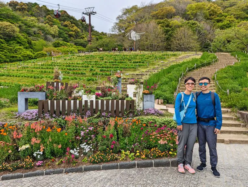 Jackie Szeto and Justin Huynh, Life Of Doing, stands in front of a flowers and garden area in the Nunobiki Herb Garden Lower Entrance