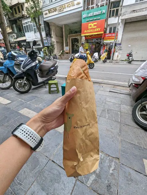A hand holding a brown bag with a hand drawn picture and a vegan Vietnamese sandwich at Banh Mi Chay Vietnam in Hanoi