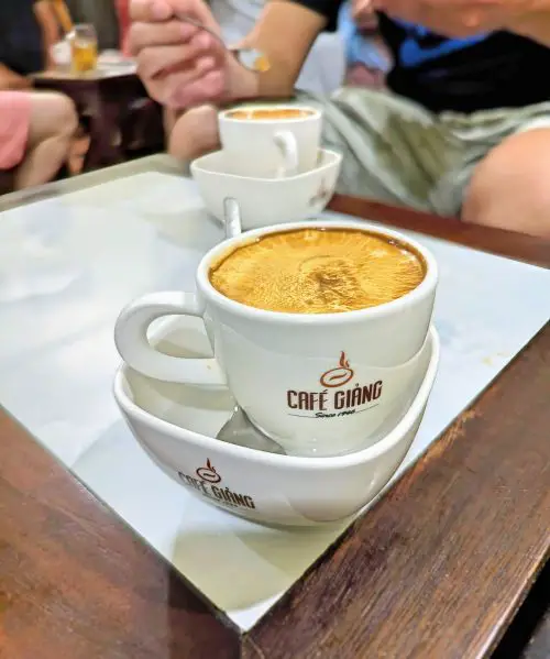 A small mug of egg coffee inside a container with warm water at Cafe Giang in Hanoi