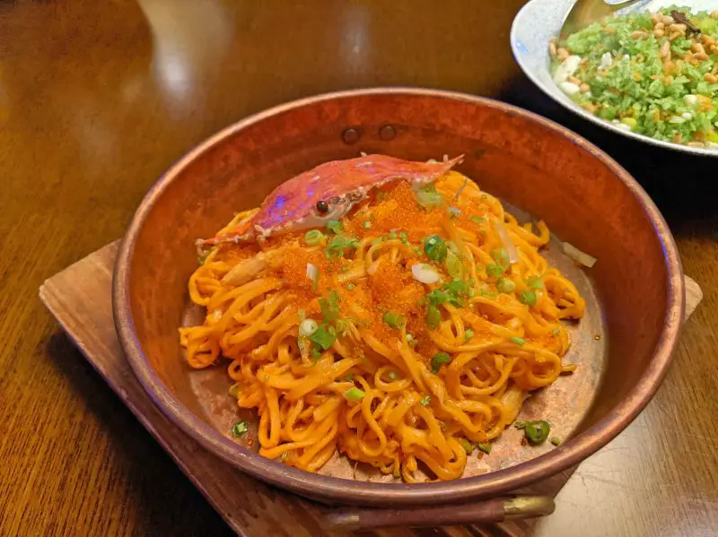 A copper bowl with orange colored yi mein noodles, fish eggs, green onions, and topped with a crab shell at Hanoi's John Anthony Cantonese Restaurant