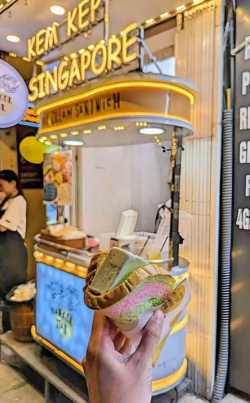 A hand holding a folded piece of bread that is pink and green and with a slice of green tea ice cream at Hawker Star in Hanoi Old Quarter