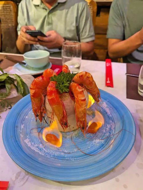 A plate of large prawns in a fresh coconut with flames surrounding the prawns at Ngon Garden in Hanoi