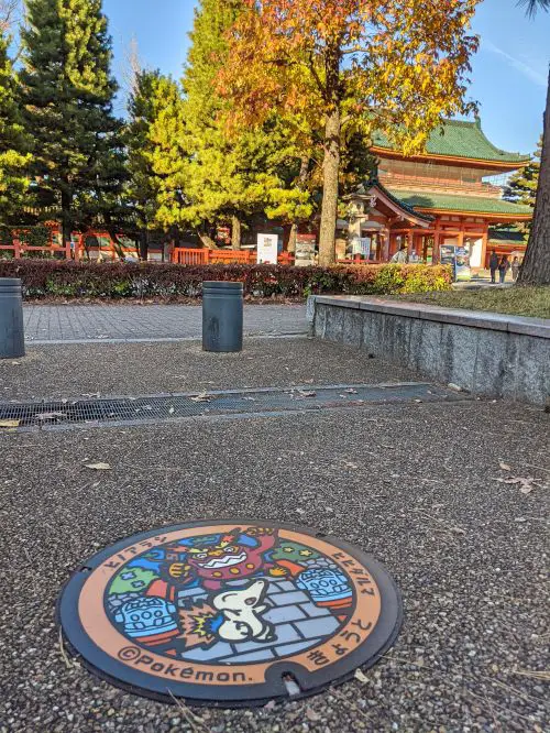 A colorful Pokemon-theme manhole cover with a temple in the background in Kyoto, Japan