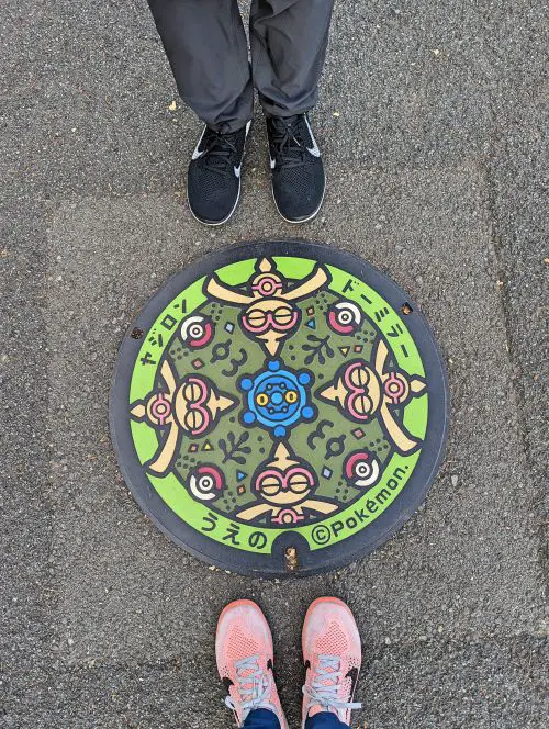 Two people's feet standing next to a Pokemon themed manhole cover in Tokyo, Japan