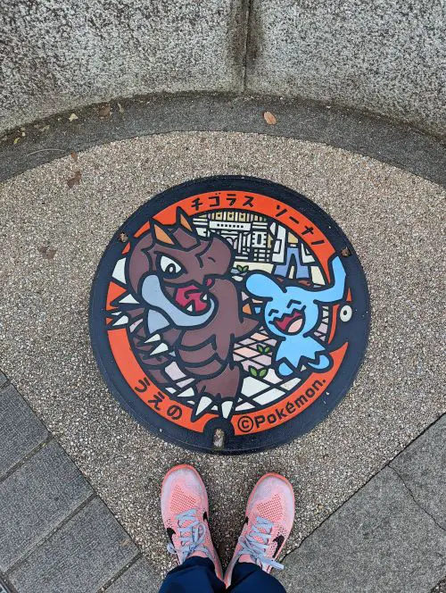 A person standing next to the Pokemon Poké Lid manhole cover with two Pokemon characters in Tokyo
