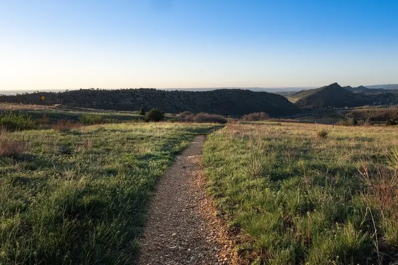 A flat hiking trail with grass growing on both sides and rolling hills