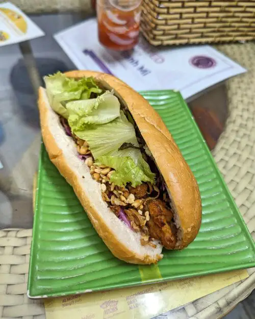 A shu mai and tofu ball banh mi sandwich with peantus and lettuce on a green plate at Vegan Banh Mi, Hanoi, Vietnam