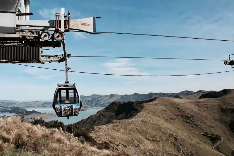 A moving gondola with a blue bay and hiking trails in the background in Christchurch, New Zealand