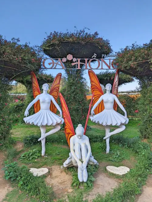 Three white ballerina statues with orange butterfly wings in front of the Hoa Hong sign at the Fansipan Cable Car Station