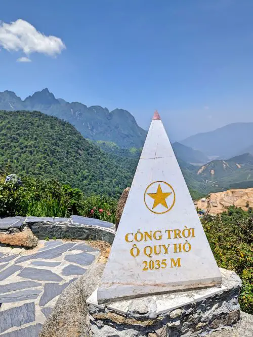 A grey triangular landmark overlooking the green mountain range of Sapa Heaven Gate on O Quy Ho Pass, Vietnam