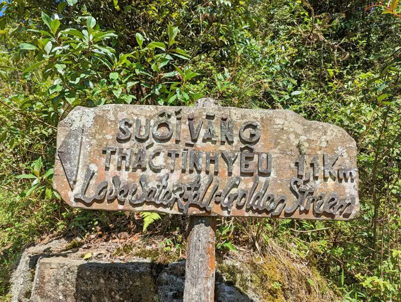 A wooden sign for Love Waterfall - Golden Stream at 1.1 kilometers away
