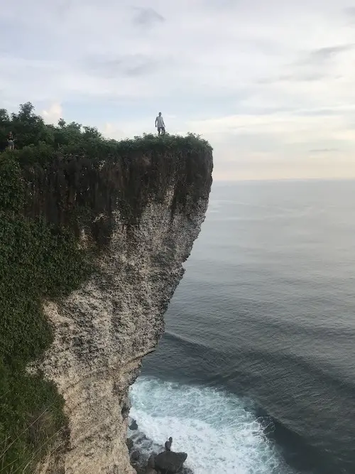 A man standing on the edge of a cliffside and overlooking the ocean in Uluwatu, Bali