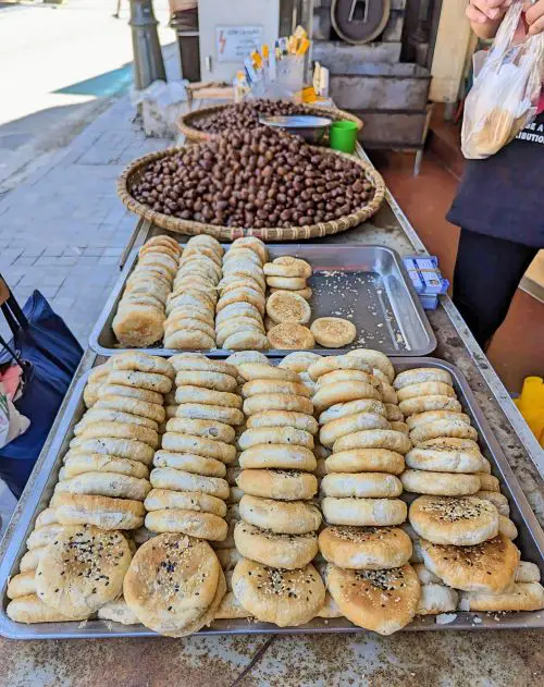 Baking trays of cooked chestnut cakes topped with black and white sesame seeds and a basket of roasted chestnuts in Sapa, Vietnam