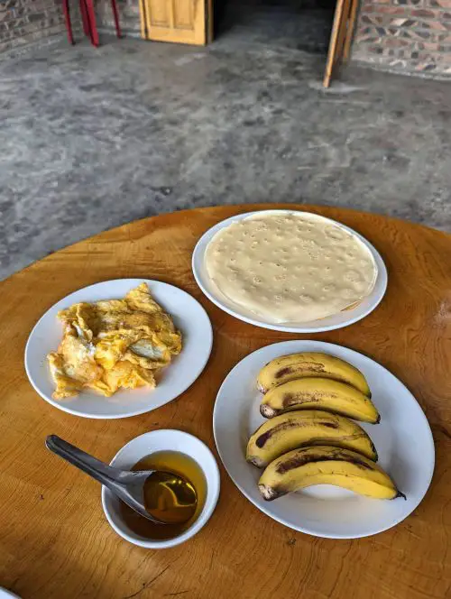 A plate of bananas, scrambled eggs, and crepes, and a bowl of honey on a wooden table at Mama Si Homestay in Sapa, Vietnam