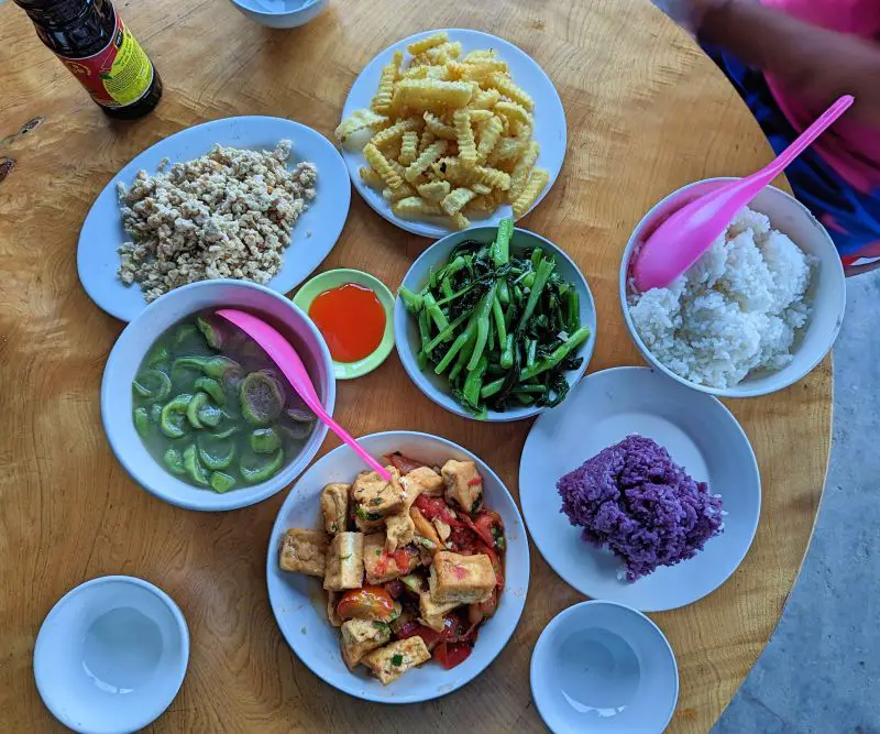 A top down photo of dinner entrees of French Fries, vegetables, tofu with tomato, squash soup, ground chicken, purple sticky rice, and white rice at Mama Si Homestay in Sapa