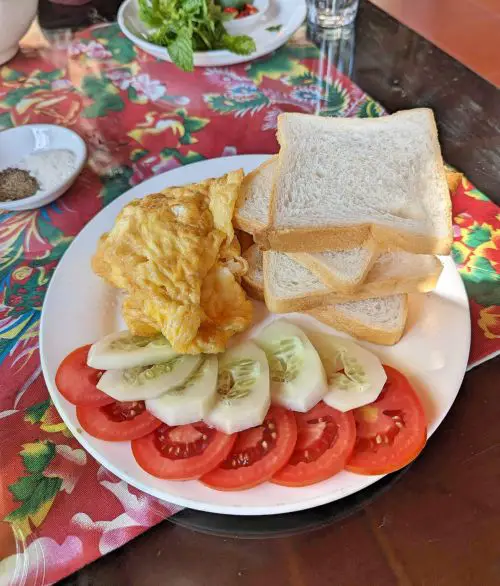 A plate of scrambled eggs, four pieces of white bread, and sliced cucumber and tomatoes at Sapa Garden Hotel