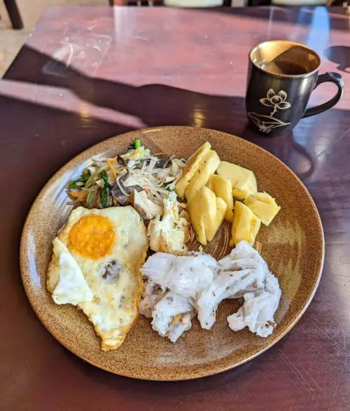 A plate of rice noodles, fried egg, pineapple slices, and vegetarian noodles for breakfast at Saparis Hotel in Sapa, Vietnam